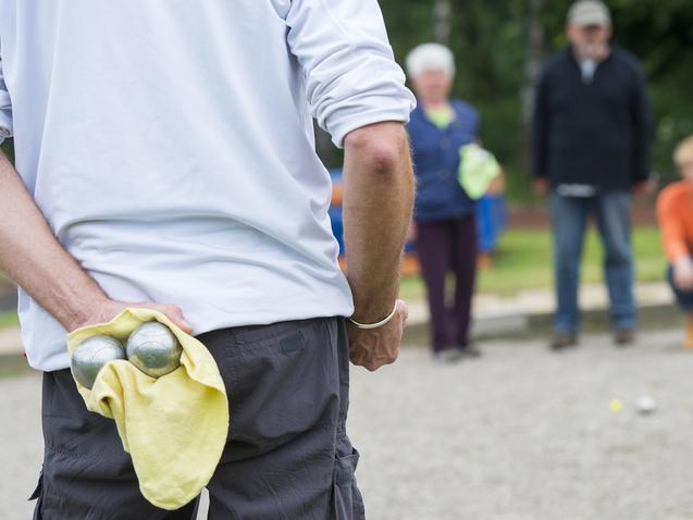 Person hält zwei Metallkugeln in einem gelben Handtuch, während andere Personen im Hintergrund zuschauen.