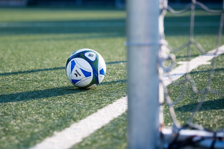 Fußball liegt auf einem Kunstrasenplatz, nahe einem Torpfosten mit Netz.