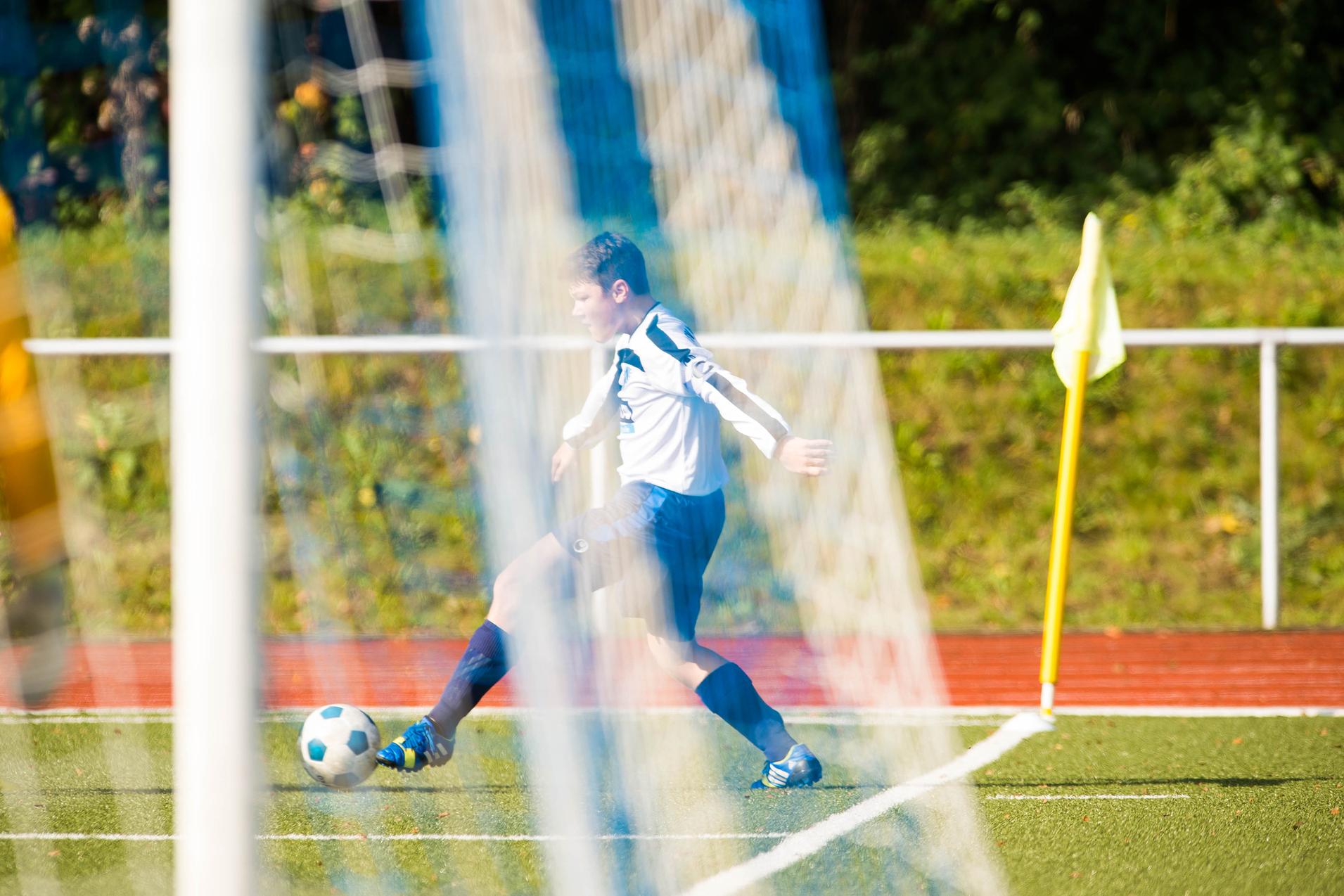 Wettkampf auf dem Fußballplatz: Ein Spieler in weiß-blauer Trikotausstattung schießt einen Ball ins Spiel.