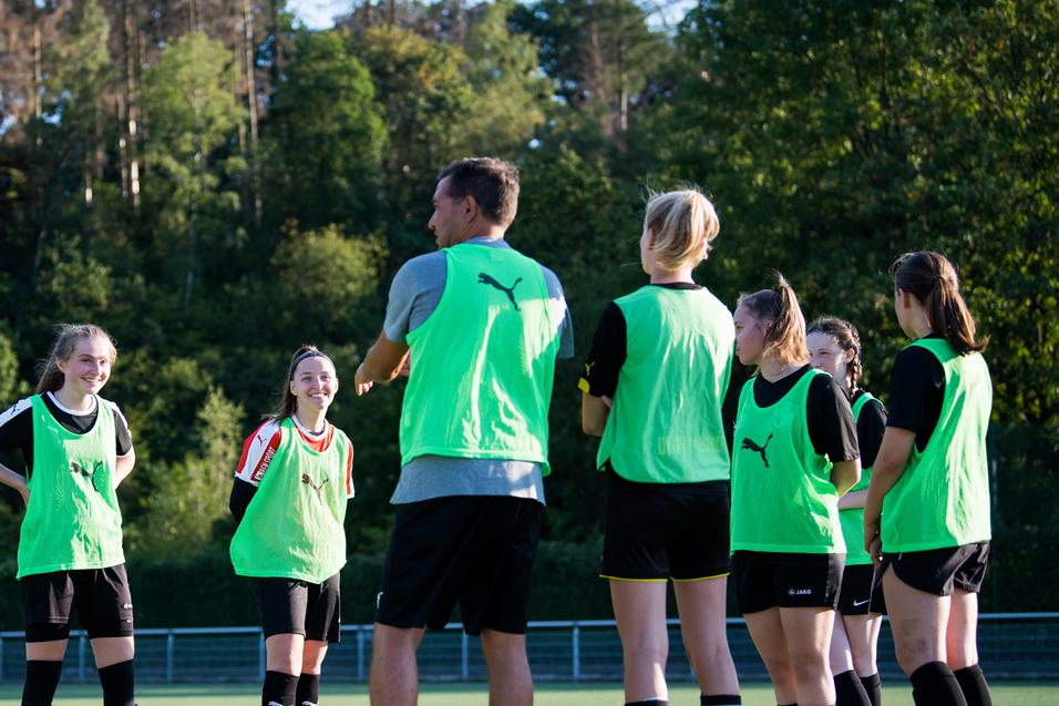 Mannschaftstraining mit Trainer: Gruppen von Mädchen tragen grüne Trainingswesten auf einem Fußballplatz.