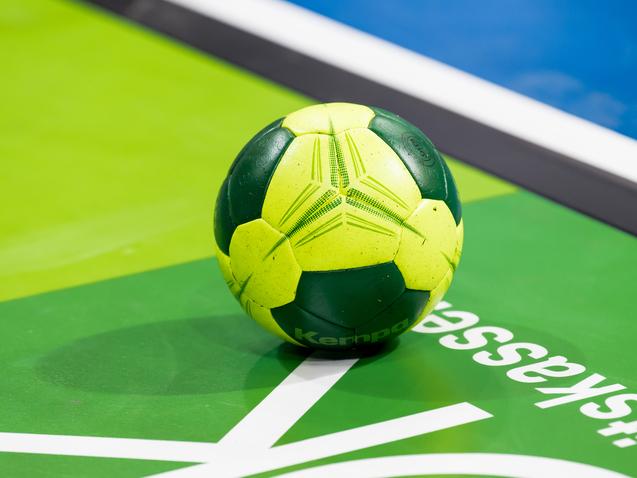 Grüner und gelber Handball liegt auf einer grünen Spielfläche mit weißem Schriftzug.