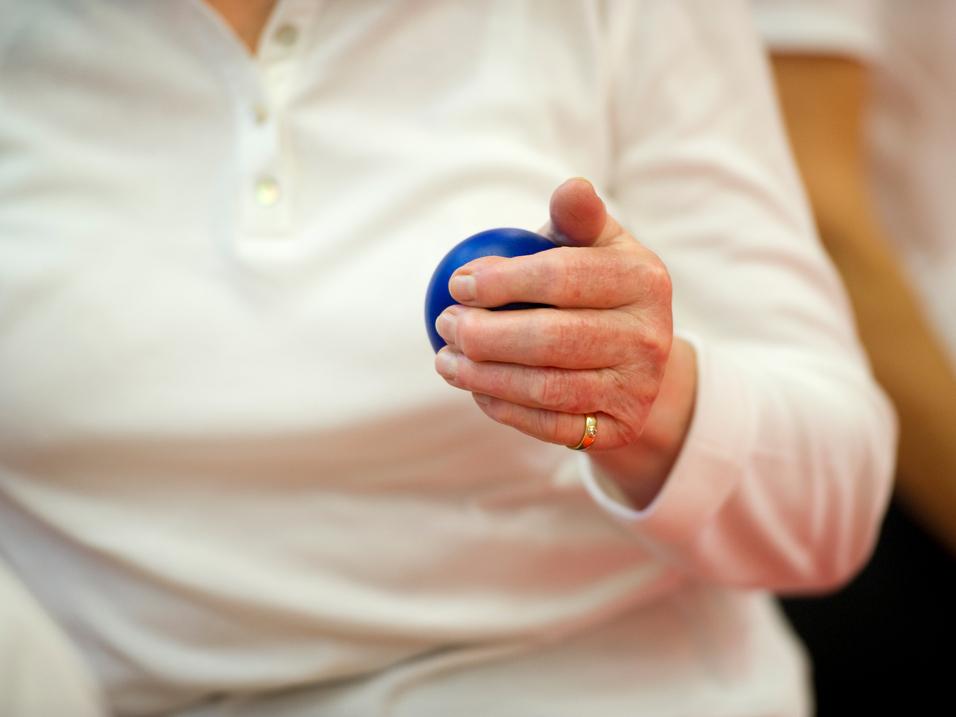 Nahaufnahme einer Hand, die einen blauen Ball hält, während die Person in einem weißen Oberteil sitzt.
