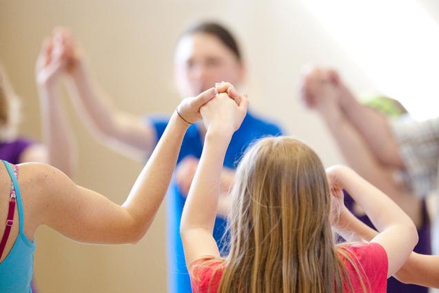 Gruppe von Kindern hält sich in einem gemeinsamen Kreis an den Händen, während sie in einer Sporthalle aktiv sind.