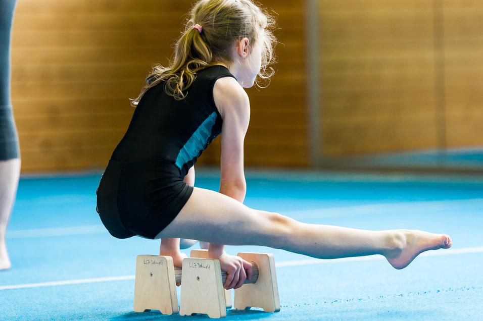 Mädchen in Turnkleidung balanciert auf Holzblöcken während des Trainings in einer Turnhalle.