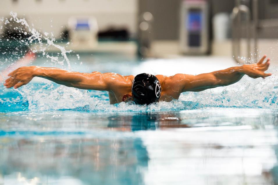 Schwimmer bei der Schmetterlingsbewegung im Wasser, Arme weit ausgebreitet, Spritzer um ihn herum.