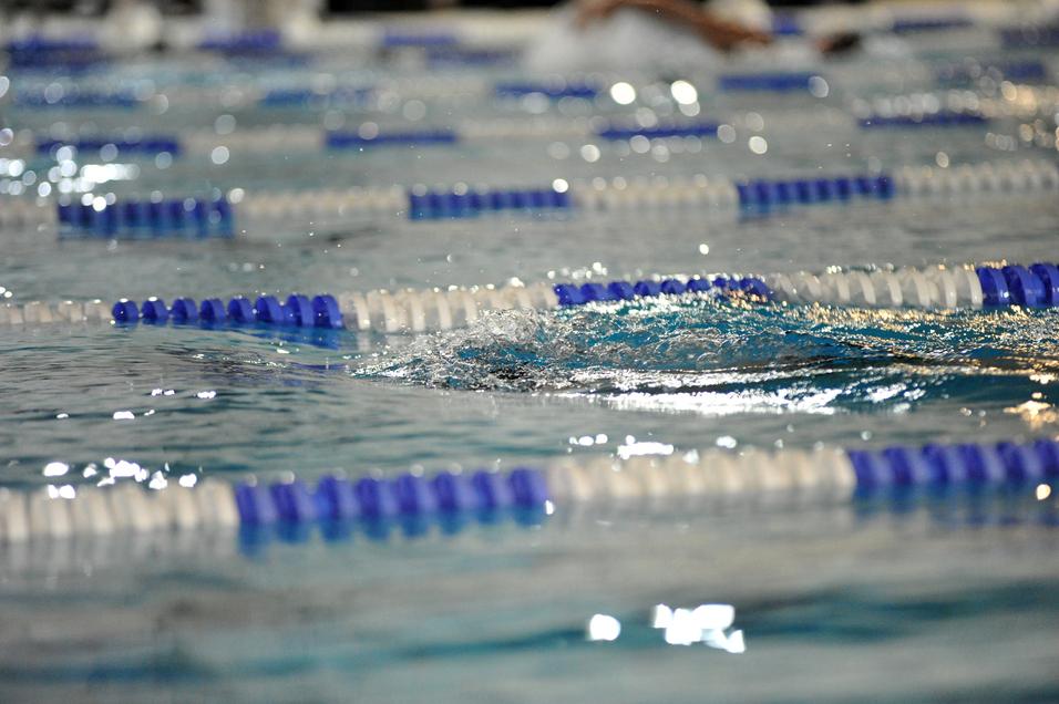 Spritzendes Wasser auf einer Schwimmbahn mit blauen und weißen Bahnmarkierungen in einem Hallenbad.