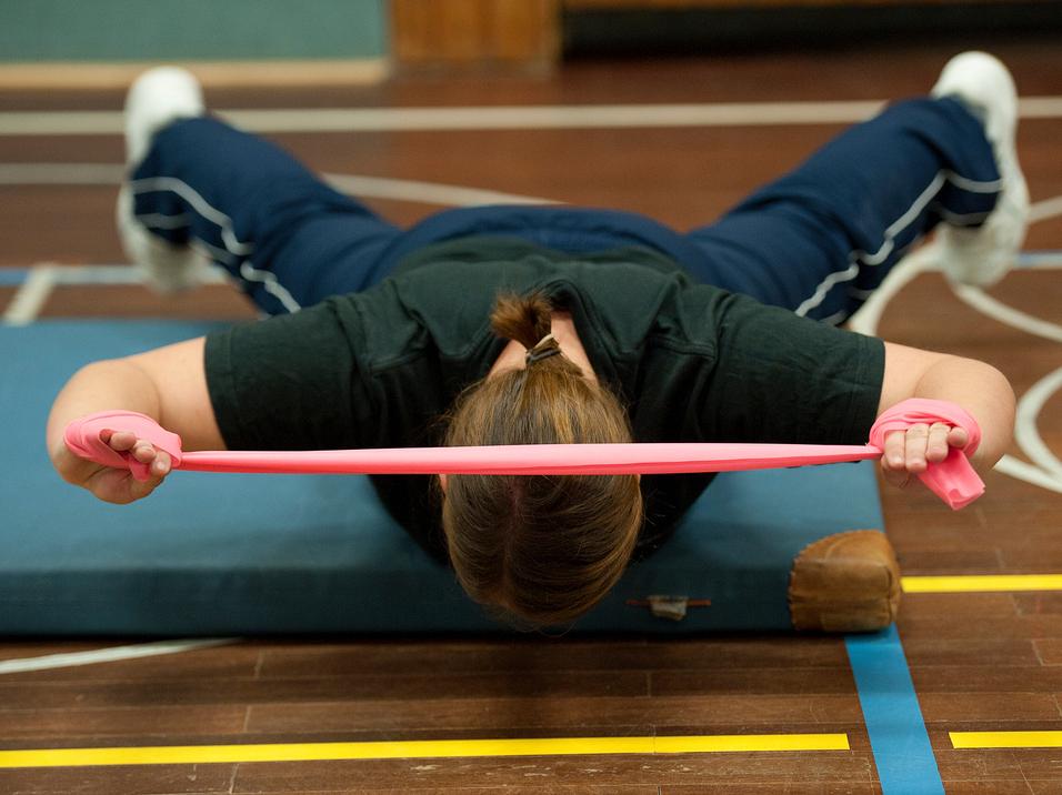 Frau führt eine Übung mit einem pinken Widerstandsband auf einer Matte in einem Sportbereich aus.