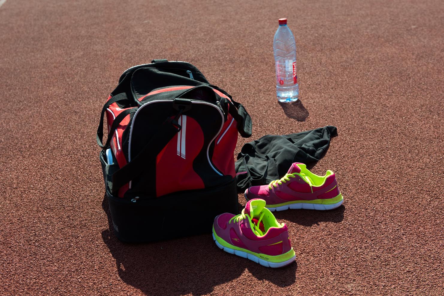 Sporttasche, pinke Sportschuhe, schwarze Kleidung und eine Wasserflasche auf einer orangefarbenen Laufbahn.